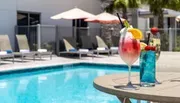 The image showcases a refreshing scene featuring two colorful cocktails on a table beside a swimming pool, conveying a sense of leisure and relaxation.