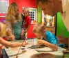 A family is engaged in an interactive exhibit with adults and children focused on an activity at a table