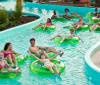Three people are enjoying a sunny day at a water park sliding down in a large inflatable ring with big smiles on their faces