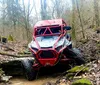 A red off-road vehicle is navigating a rocky creek bed with a person visible behind the roll bars engaged in an outdoor adventure