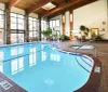 This image shows an indoor swimming pool area with lounge chairs large windows and a hot tub reflecting a leisurely and comfortable atmosphere
