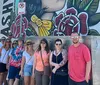 A group of people is posing for a photo in front of a large mural with vibrant artwork on a sunny day