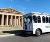 A trolley-style bus marked Music City BrewHop is parked in front of a building with classical Greek architecture