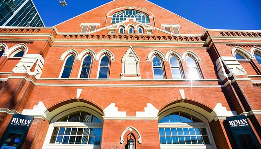 The image shows the exterior of the Ryman Auditorium, with its distinctive red brick architecture, arched windows, and signage.