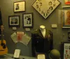The image shows a display case with various music memorabilia including a decorative guitar photographs clothing a cowboy hat and hand-written notes suggesting a tribute to a musicians career