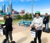 Two individuals are smiling for the camera while riding Segways on a path with the Nashville skyline in the background