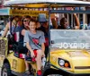 A group of people is enjoying a tour on a unique golf cart-like vehicle labeled JOYRIDE on a vibrant city street