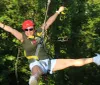 A person is gleefully experiencing a zipline adventure among the trees wearing a helmet and a harness for safety