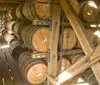 The image shows a collection of wooden barrels possibly containing whiskey or wine aging in a storage rack within a dimly lit warehouse