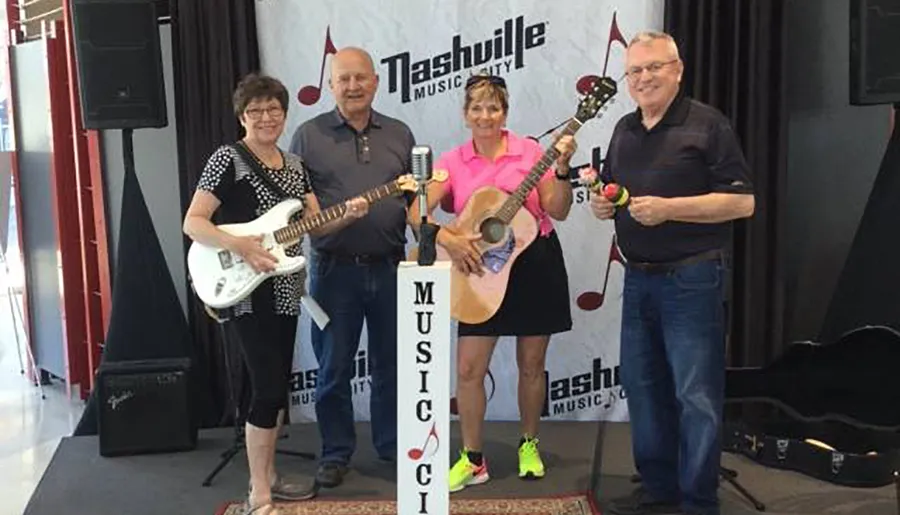 Four individuals are posing on a stage with musical instruments, likely a band preparing for or after having performed, in front of a Nashville Music City backdrop.