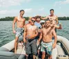 A group of cheerful men in swimwear are having a good time on a boat some holding beverages on a sunny day