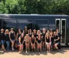 A group of people is posing for a photo in front of a black bus on a sunny day