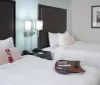 The image shows a neatly arranged modern hotel room with two beds side tables lamps and a framed picture on the wall
