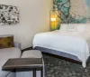 The image shows a neatly arranged hotel room with a large bed a sofa with patterned cushions abstract artwork and modern lighting