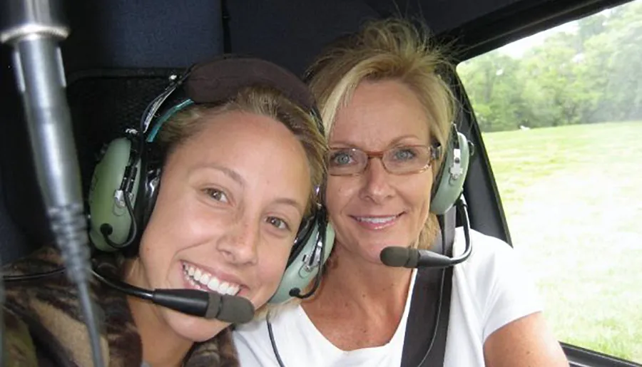 Two people are smiling for a selfie while wearing aviation headsets, possibly inside an aircraft.