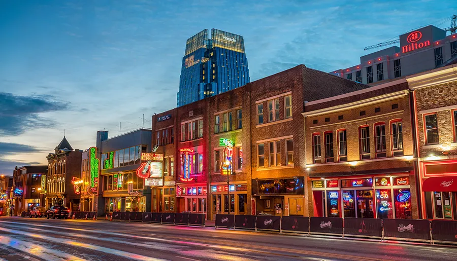 The image shows a vibrant street lined with neon signs and historic buildings at dusk, reflecting the lively atmosphere of an urban entertainment district.