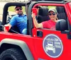 Two people are smiling and enjoying a ride in a red Jeep with a Top Down Tours Nashville decal on the side suggesting a leisurely tour experience