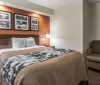 The image shows a neatly arranged hotel room with two double beds a nightstand with a lamp framed artwork on the wall and warm-colored decor