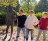 Three men mimic the pose of a statue standing confidently with hands on hips in a sunny outdoor setting