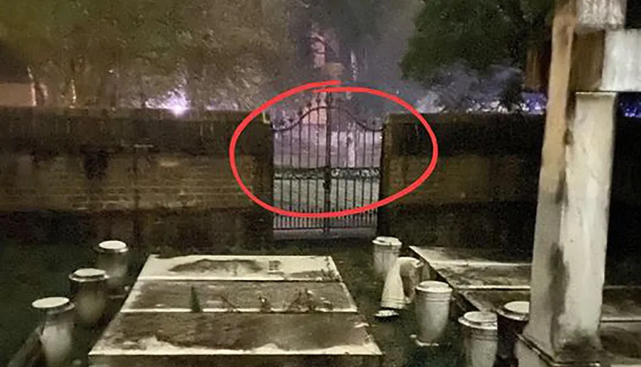 The image features a dimly lit outdoor scene with a red circle highlighting an area behind a gate, where a faint, blurred silhouette of a figure appears, creating a spooky or mysterious atmosphere.