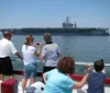 A tour boat named Miss Hampton II is cruising near a large naval aircraft carrier in a harbor