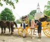Two people are interacting with a carriage driver dressed in historical attire before a bright yellow horse-drawn carriage with architectural and natural elements suggesting the scene may be set in a historical or tourist location