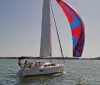 A sailboat with a colorful spinnaker sails on a sunlit body of water