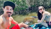 A smiling man and woman are enjoying kayaking together, with a manatee visible in the water near them.