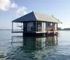 A quaint wooden cabin floats on calm water featuring a porch with a hanging hammock