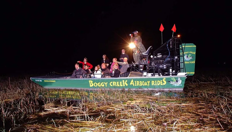 A group of people enjoy a nighttime airboat tour in a marshy area.