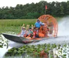 A group of people are joyfully waving while riding an airboat through a waterway with lush greenery on the sides