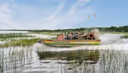 An airboat carrying passengers glides through a marshy landscape with the text 