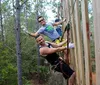 Three people are climbing a tall wooden structure outdoors secured with harnesses and ropes displaying expressions of enjoyment and adventure