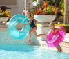 Two children are joyfully jumping into a swimming pool with inflatable tubes