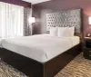 The image shows a neatly made bed with white bedding in a modern and stylish hotel room with a patterned carpet purple walls and minimalist furniture