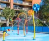 A colorful childrens splash pad with various water features is situated in front of a multi-story building with balconies
