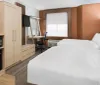 The image shows a modern hotel room with a bed work desk area seating space and abstract wall art combining a functional design with a touch of vibrant colors