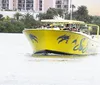 A bright yellow boat with dolphin graphics and the name SunShine sails with passengers on board set against a backdrop of lush greenery and urban buildings