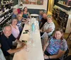 A group of people is smiling and posing for a photo at a long table in a cozy wine shop or bar