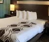 The image shows a neatly made bed with a geometric-patterned comforter in a well-appointed hotel room
