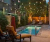 The image shows a cozy evening setting with a small illuminated pool surrounded by reclining chairs string lights and an inviting fire pit area creating a tranquil backyard ambiance