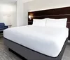 The image shows a neatly arranged modern hotel room with a large bed a blue sofa and abstract wall art