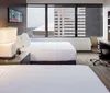 This image shows a modern hotel room with two beds a work desk a large window with a city view and contemporary furnishings