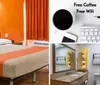 The image shows a simple hotel room with one double bed and two single beds featuring orange walls and minimal furnishings