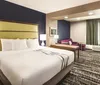 The image shows a modern hotel room with a large bed a seating area and contemporary decor