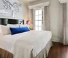 The image shows a neatly made bed with white linens and a blue accent pillow in a room with brick walls and a large butterfly artwork above the bed