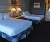 The image shows a tidy hotel room with two beds nightstands with lamps artworks on the wall and an entrance to the bathroom