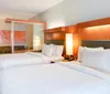 The image shows a modern hotel room with two double beds a seating area in the background and warm lighting creating a welcoming ambiance