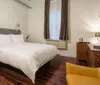 The image shows a modern and stylish hotel room with brick walls a large bed chic furnishings and plenty of natural light