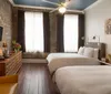 The image shows a modern and stylish hotel room with brick walls a large bed chic furnishings and plenty of natural light